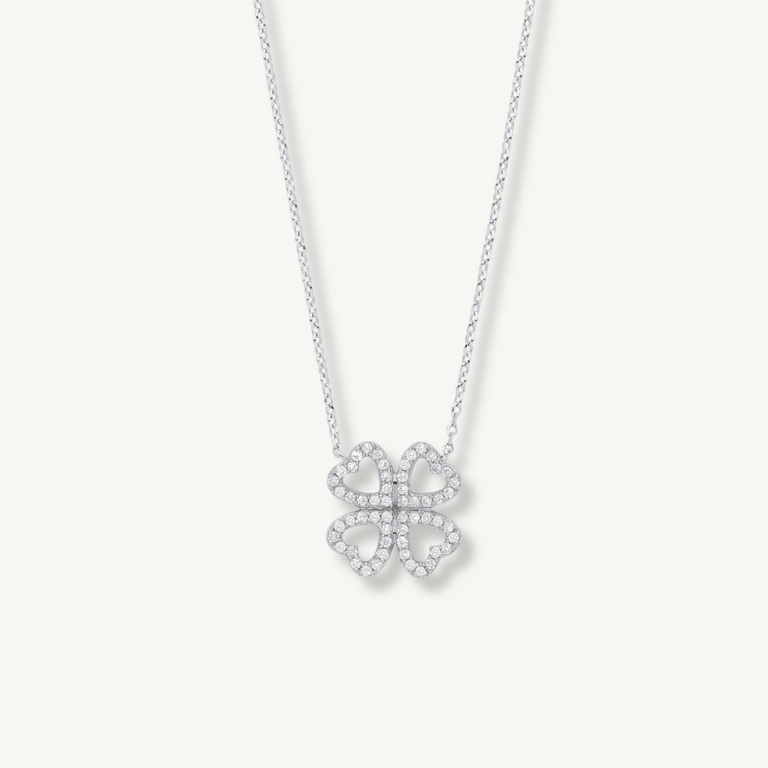 A delicate silver chain necklace featuring a small four-leaf clover pendant paved with clear stones, displayed against a solid off-white background.