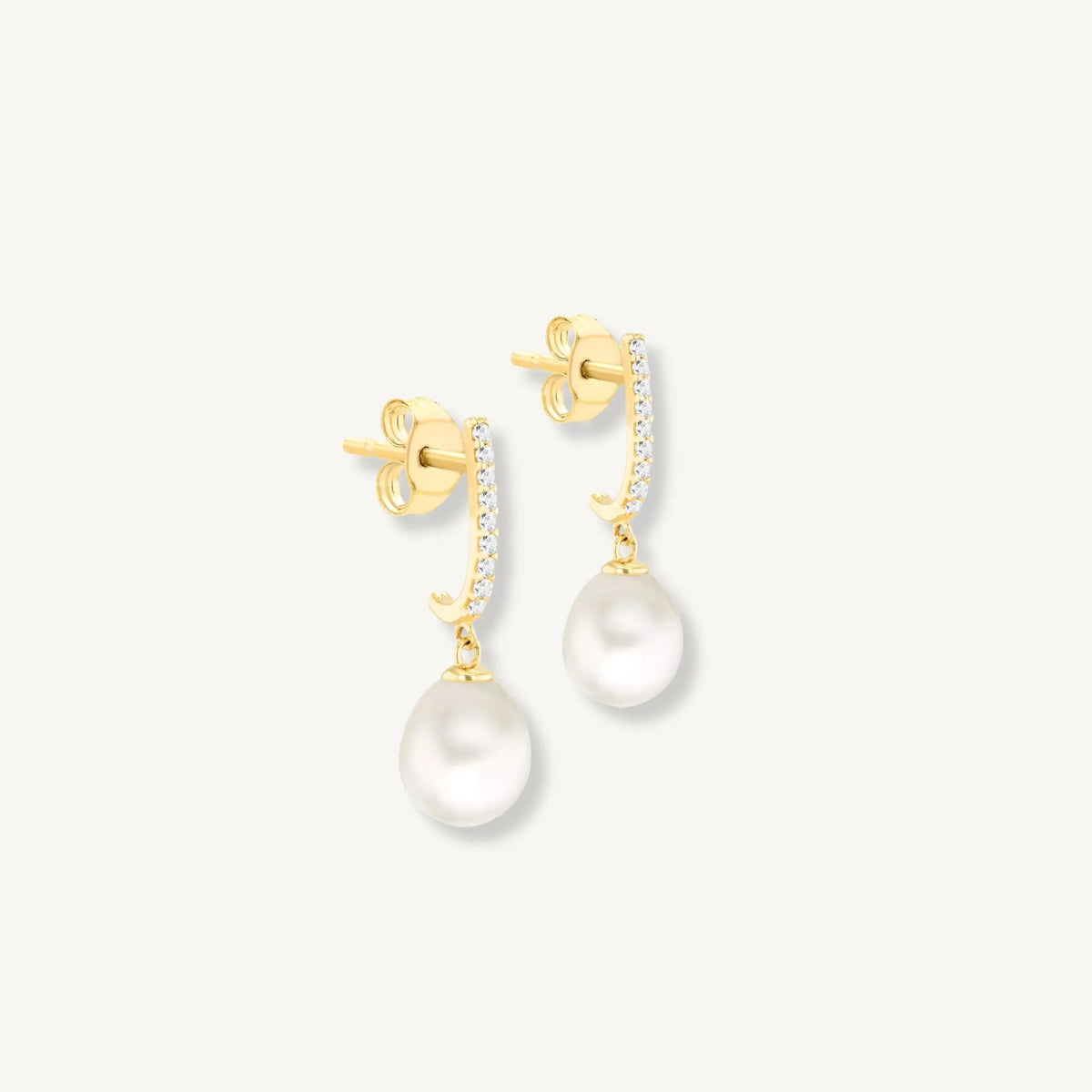 Gold earrings with pearl drops on a light gray background