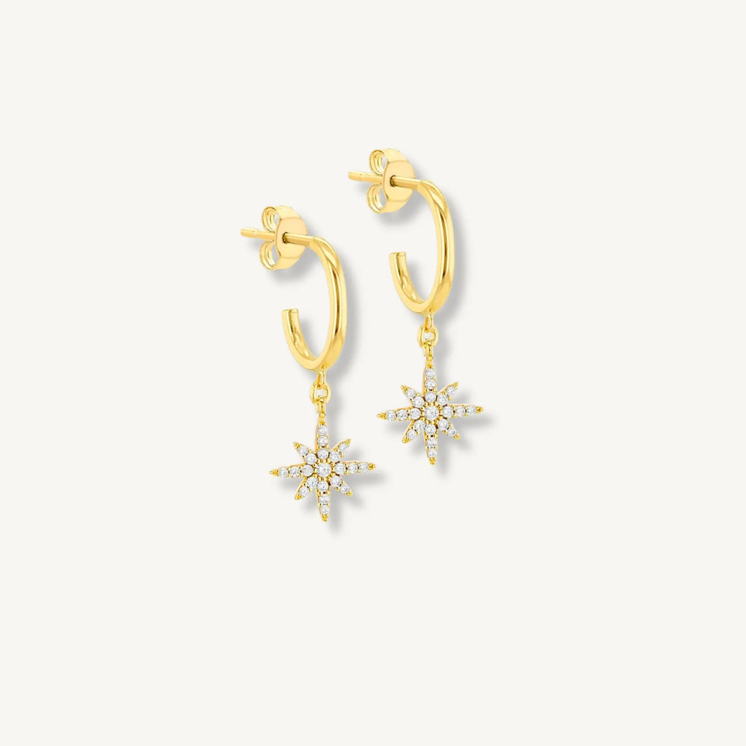 Gold hoop earrings with snowflake charms on a light gray background