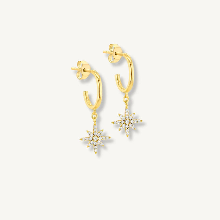 Gold hoop earrings with snowflake charms on a light gray background