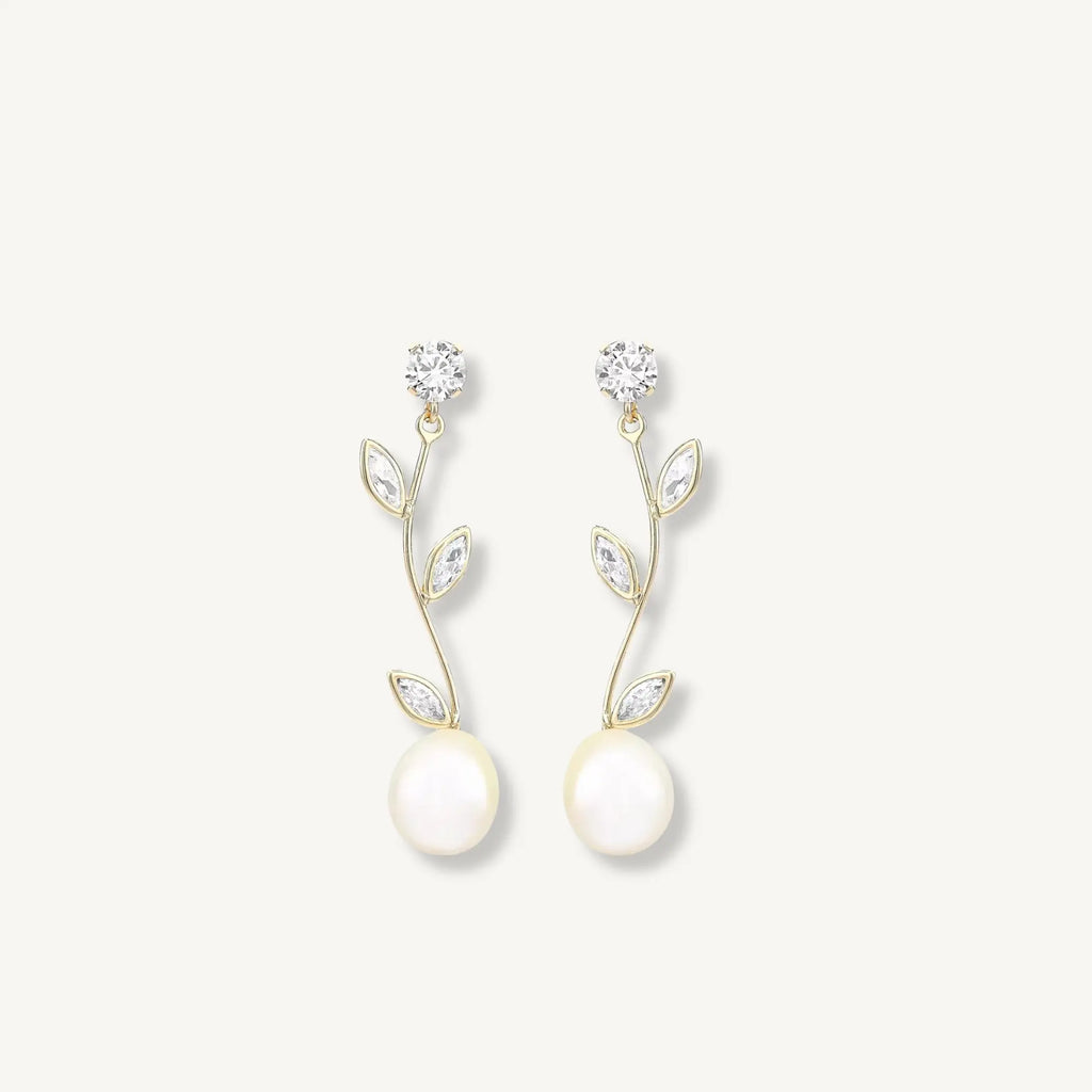 Pair of pearl earrings with gold leaves and clear stones on a light gray background
