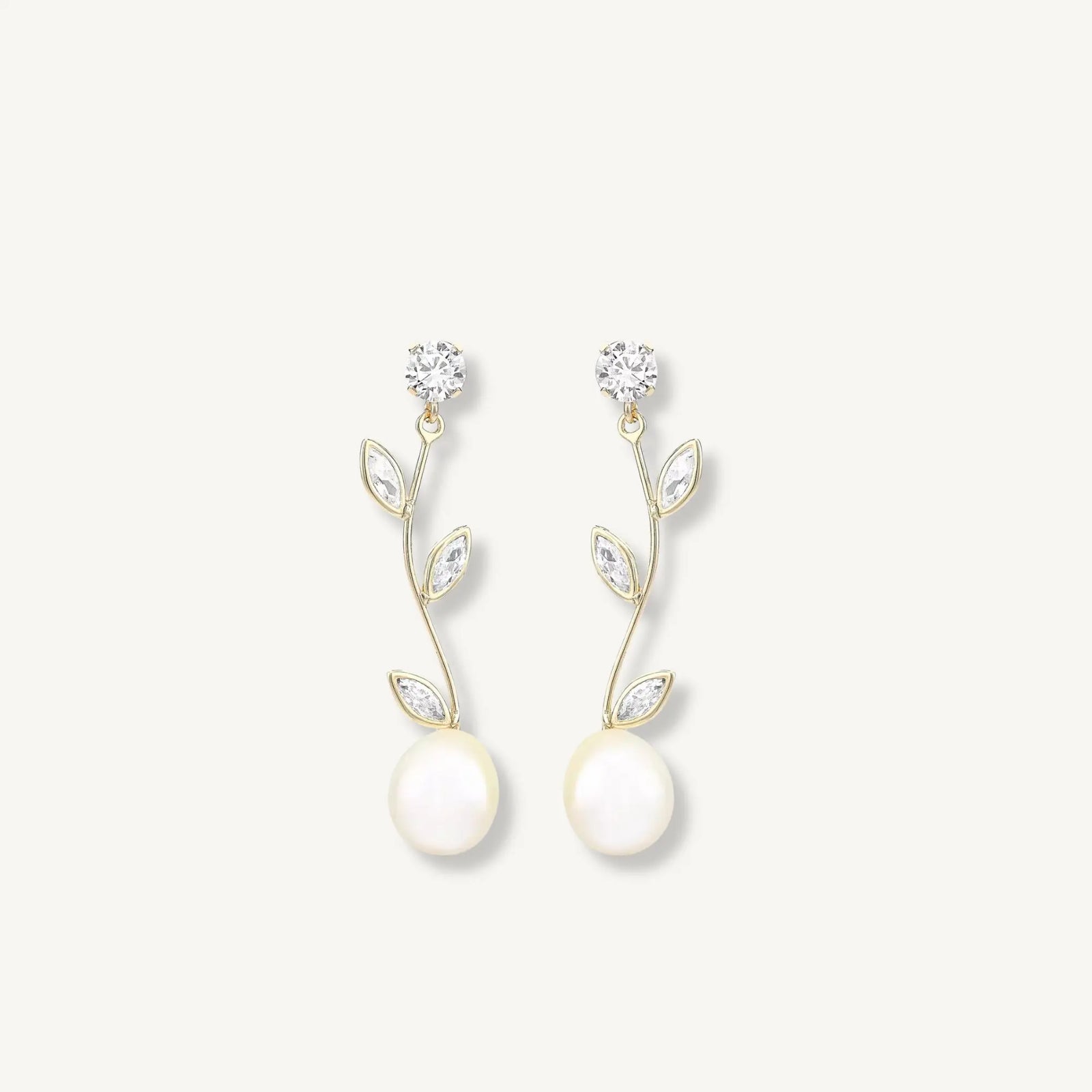 Pair of pearl earrings with gold leaves and clear stones on a light gray background
